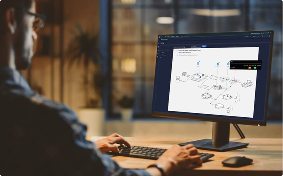 Person working at a desk with a computer monitor displaying a network topology diagram and configuration interface in a modern office setting