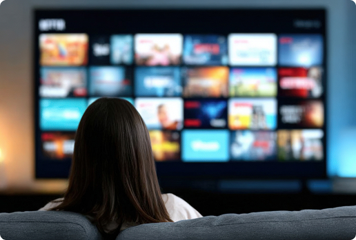 Person sitting on a couch facing a large television screen displaying a grid of streaming service thumbnails and content options in a home entertainment setting