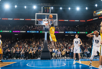 Basketball player in a yellow uniform performing a slam dunk during a professional game, with opposing team players in white uniforms and a cheering crowd in the background