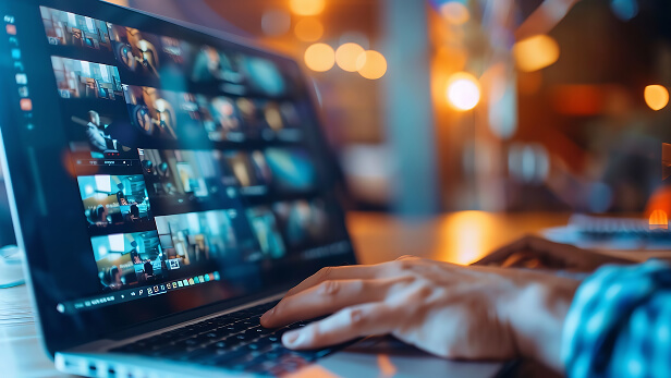 Close-up of a laptop screen displaying multiple video thumbnails in a grid layout, with a person’s hand on the keyboard, suggesting video review or quality control in a modern workspace